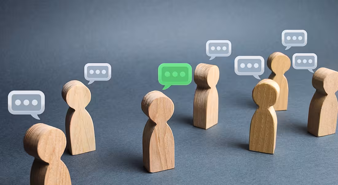 Small wooden figures have speech bubbles over their heads on a grey background.