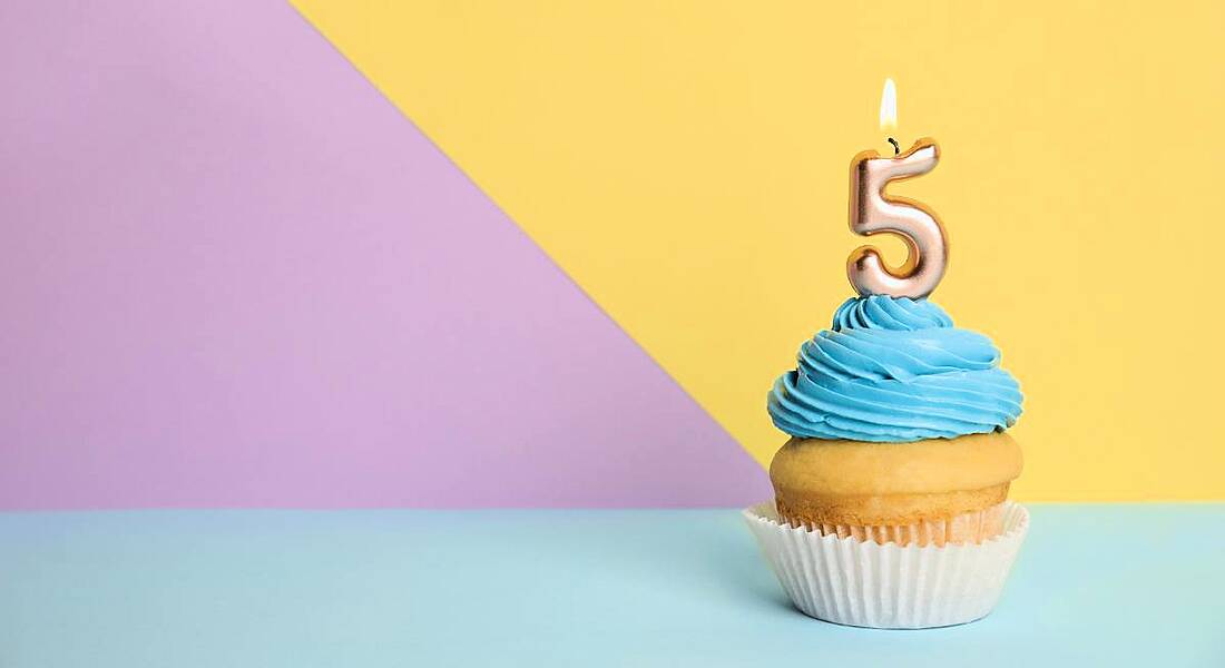 Birthday cupcake with number five candle on colourful background.