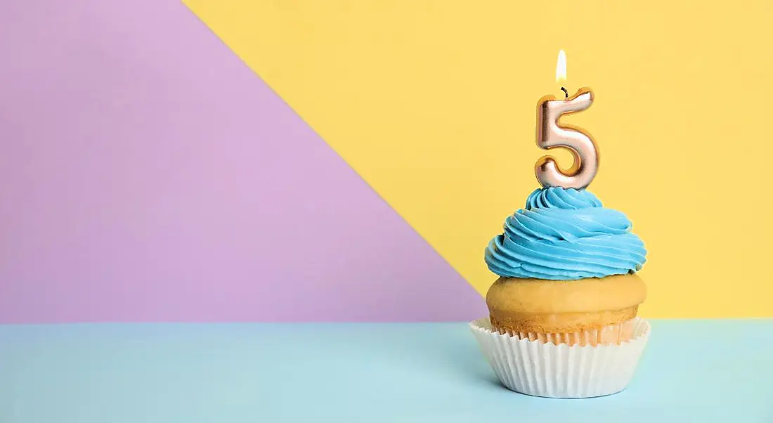 Birthday cupcake with number five candle on colourful background.