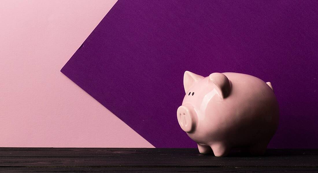 A piggy bank is standing on a dark wooden table against a pink and purple background.