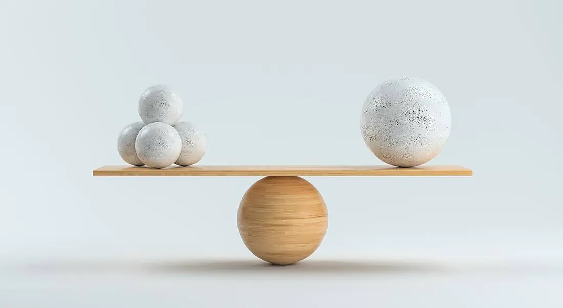 A wooden board bearing three stone balls on one side and one large ball on the other is perfectly balance atop a wooden sphere.