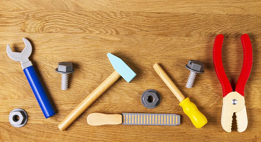 Flat lay of toy tools including a screwdriver, plier, bolts, nuts and a hammer on a wooden table.