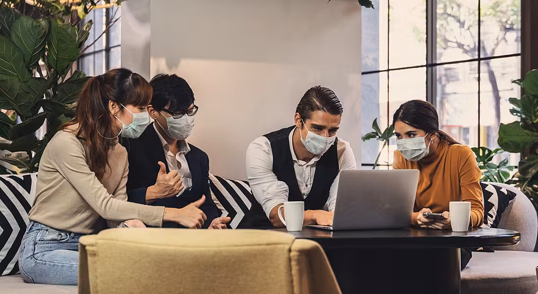 A group of colleagues are wearing face masks at work in a casual office space.