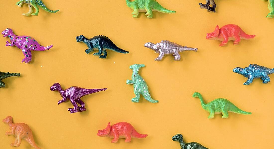 Colourful toy dinosaurs are laying against a light orange background.