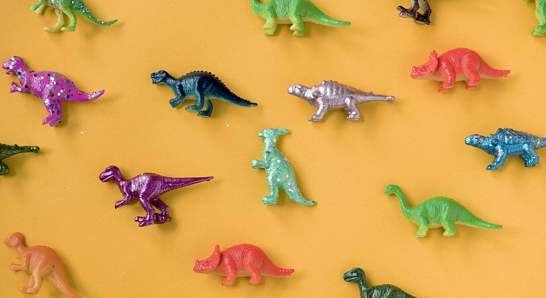 Colourful toy dinosaurs are laying against a light orange background.