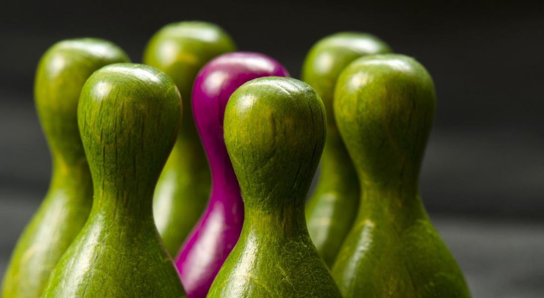 Green wooden figurines are grouped around a pink wooden figurines, symbolising discrimination and unconscious bias training.