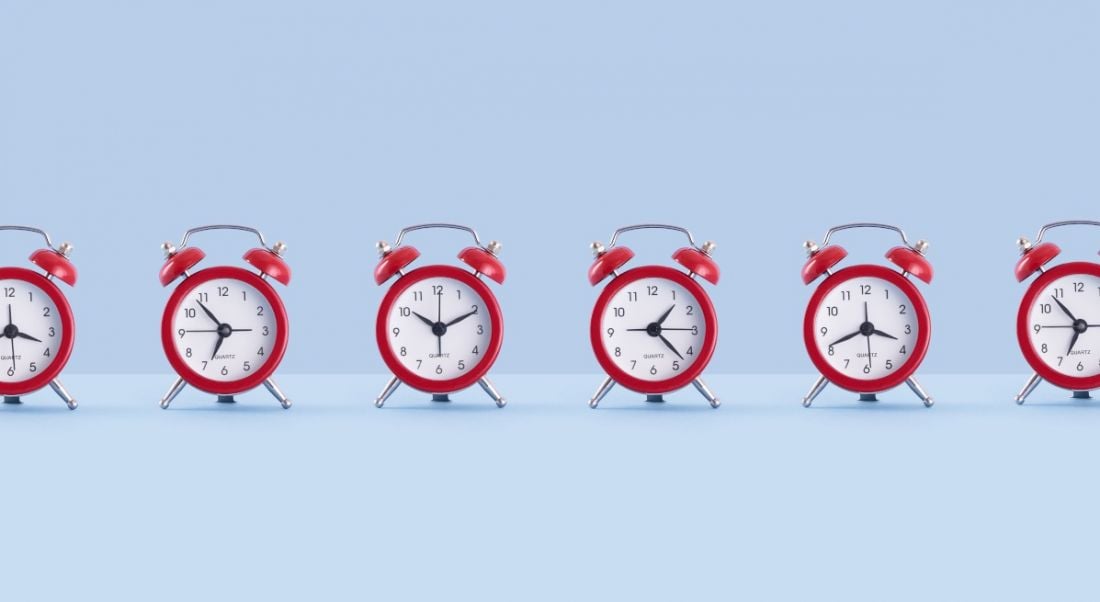 A line of small red alarm clocks against a blue background, all showing different times.