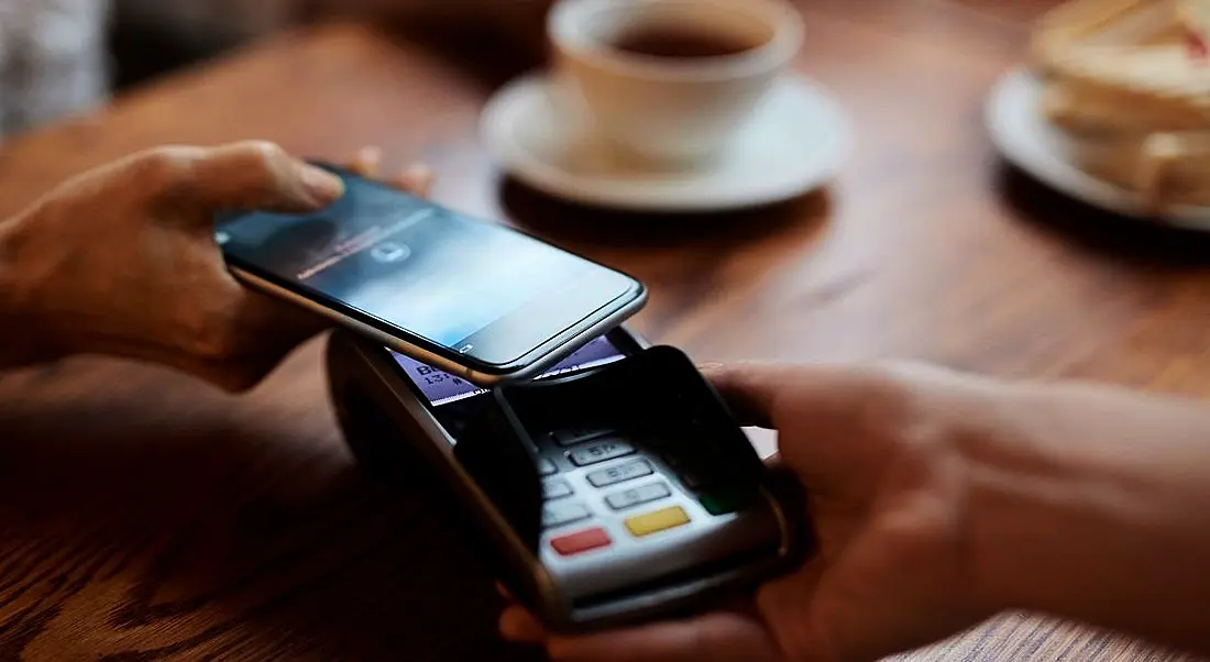 Person holding their phone at a terminal to pay for their coffee.