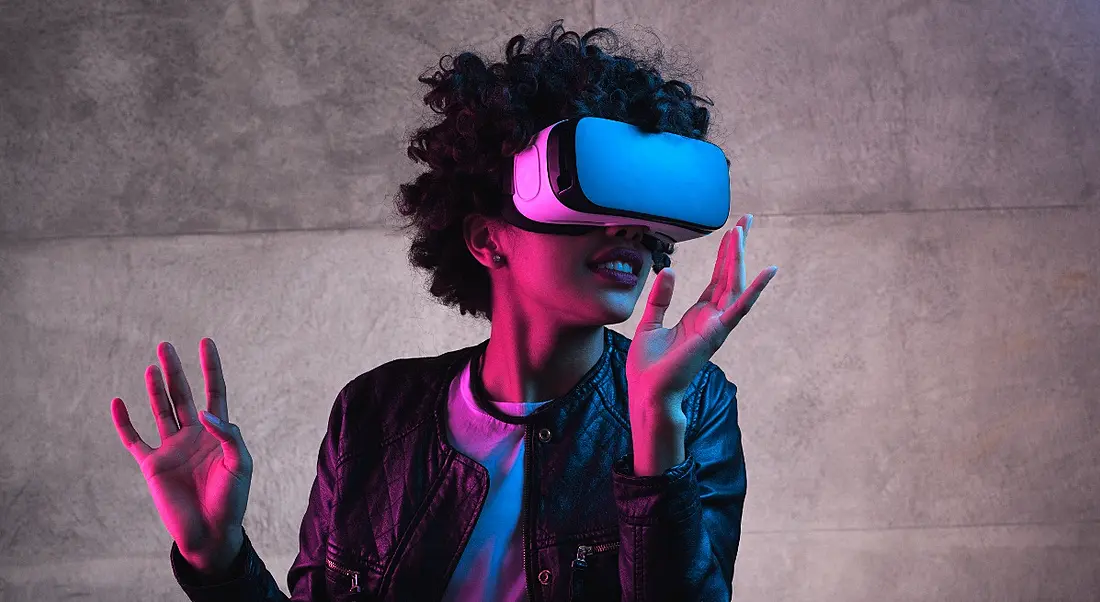 A woman is lit up by pink lighting and wearing a virtual-reality headset.