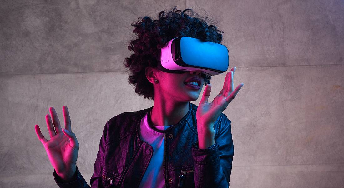 A woman is lit up by pink lighting and wearing a virtual-reality headset.