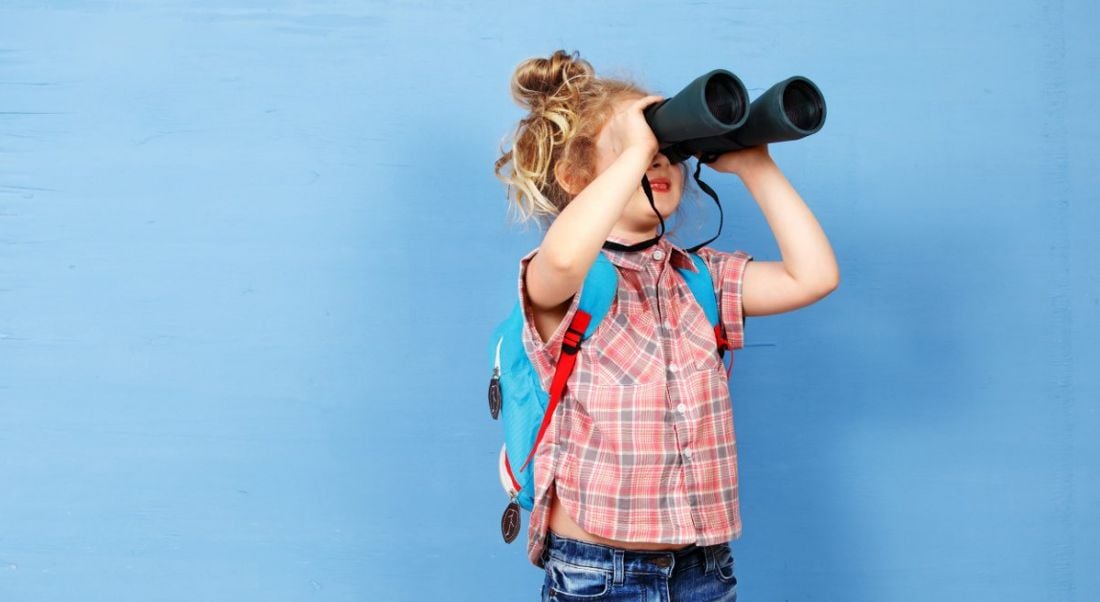 A young girl is looking through binoculars against a blue background, symbolising a job hunt.