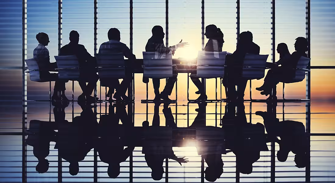Silhouettes of board members meeting in a room at sunset.