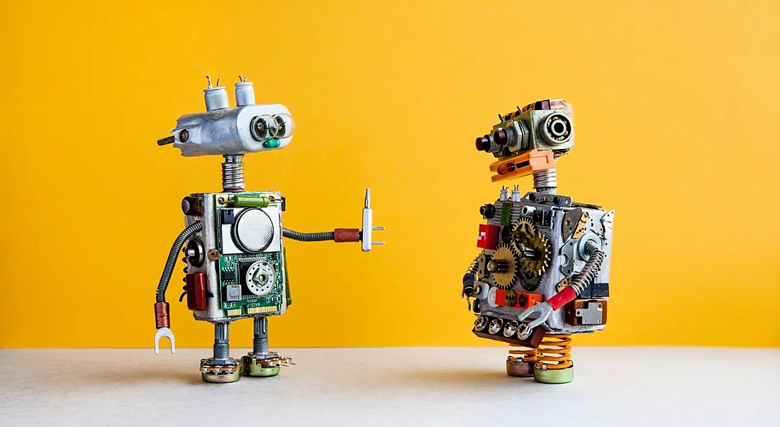 Two toy robots are talking to each other against a yellow background.