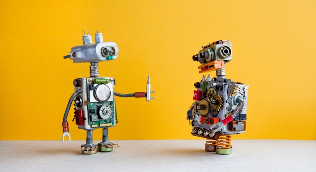 Two toy robots are talking to each other against a yellow background.