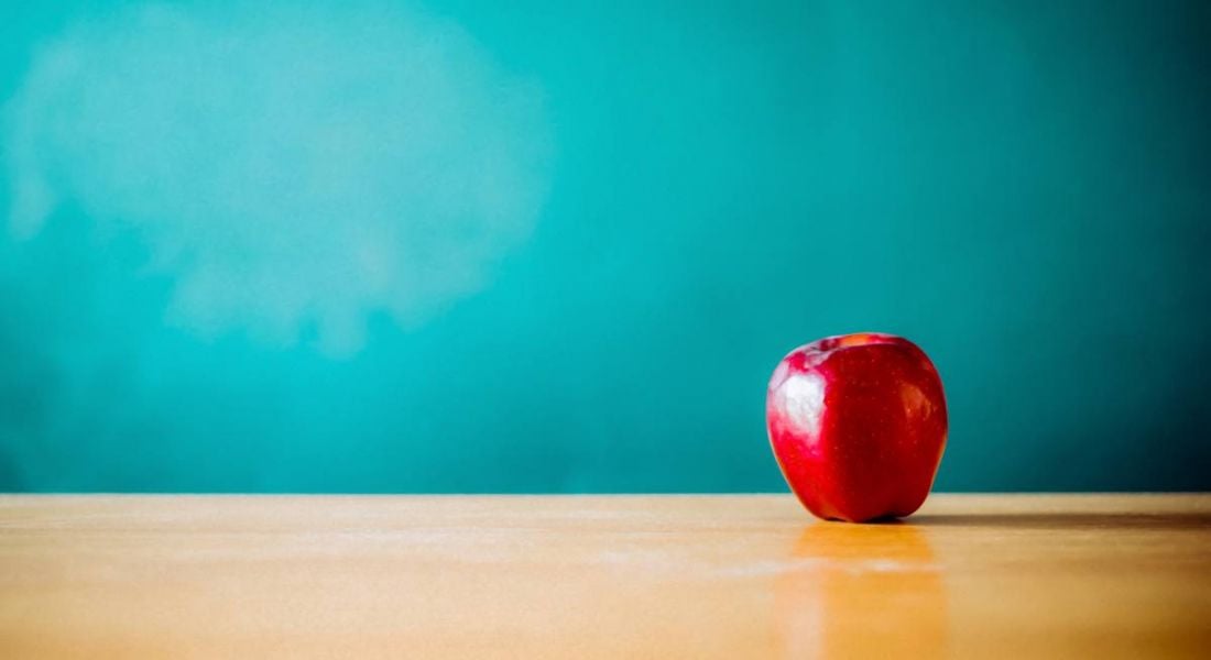 A red apple is on top of a teacher's desk in front of a blackboard.