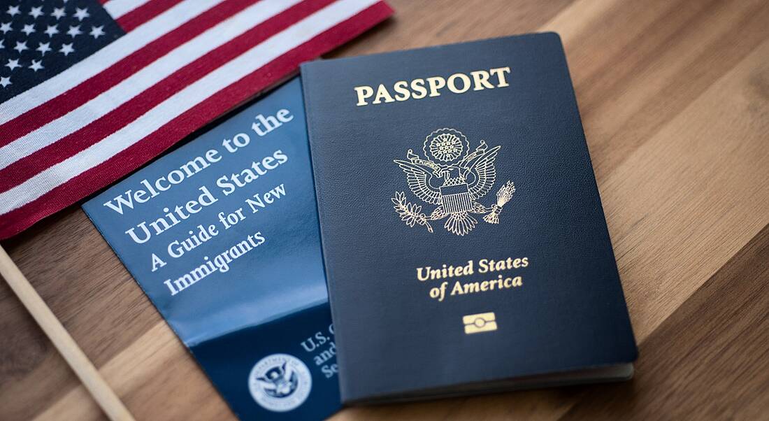 US passport next to a guide for people relocating to the country and the US flag on a wooden table.