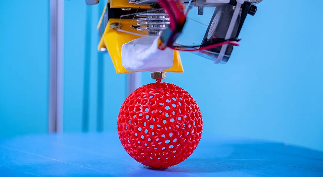 3D printing a red sphere in industrial lab against a blue background.