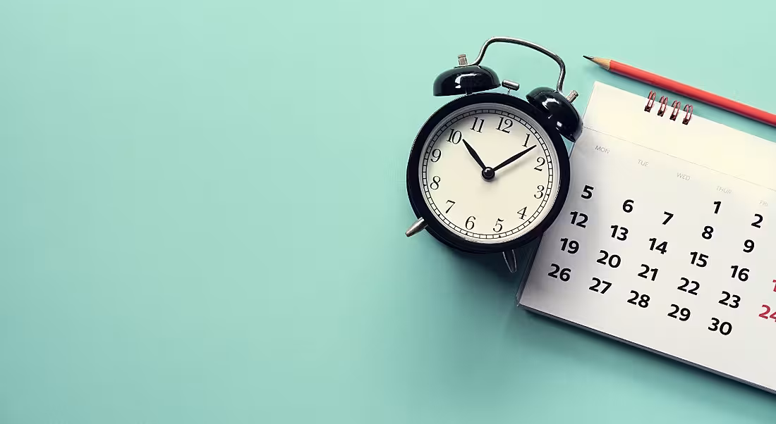Close-up of calendar and alarm clock on green background.