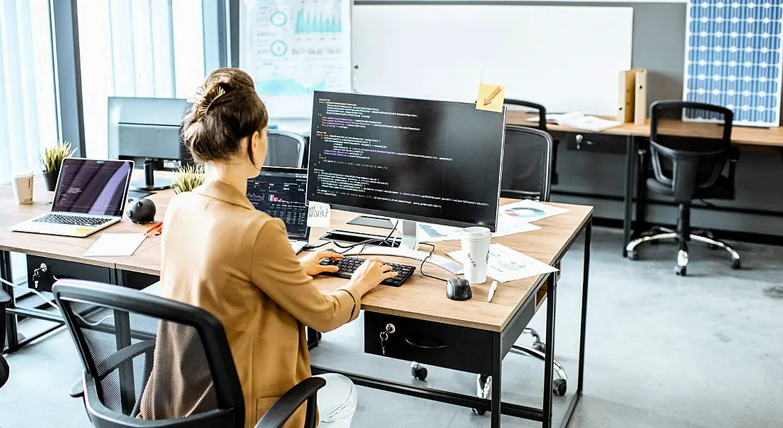 A woman is typing code on a computer in a workplace.