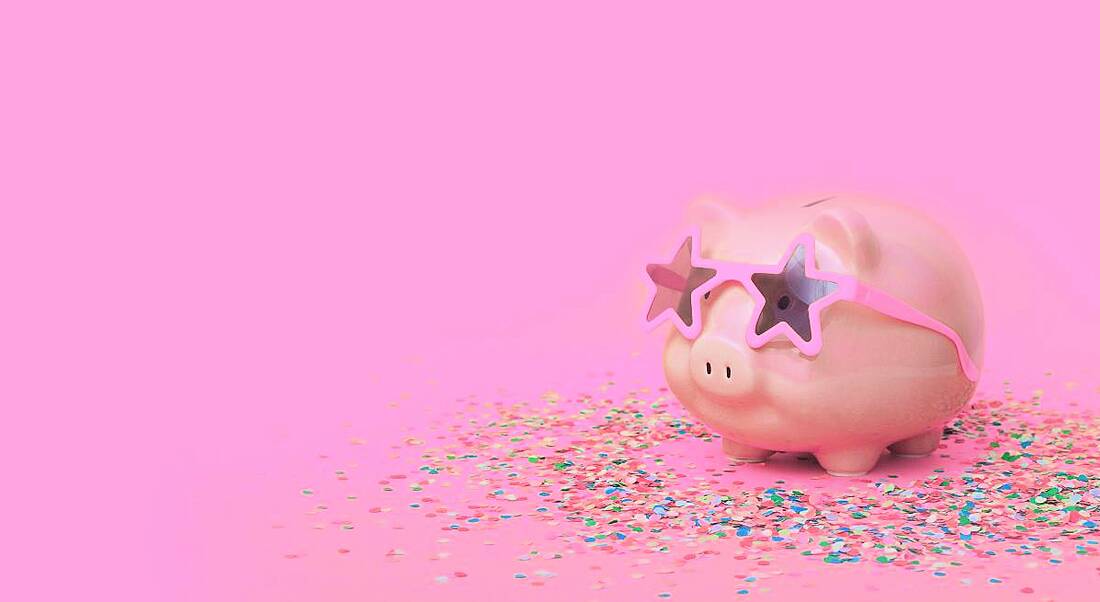 Pink piggy bank with confetti and star-shaped sunglasses on a pink background, symbolising financial wellbeing.