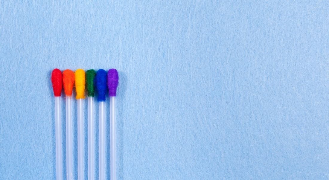 Rainbow-coloured cotton buds against a blue background, symbolising diversity and inclusion.