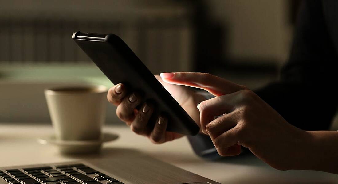 An employee is sitting at a desk with a laptop and a cup of coffee, while using a mobile phone.