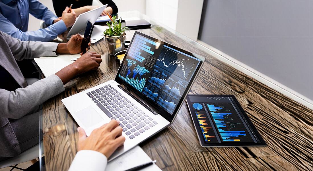 A team is working on data analytics on laptops on a wooden desk.