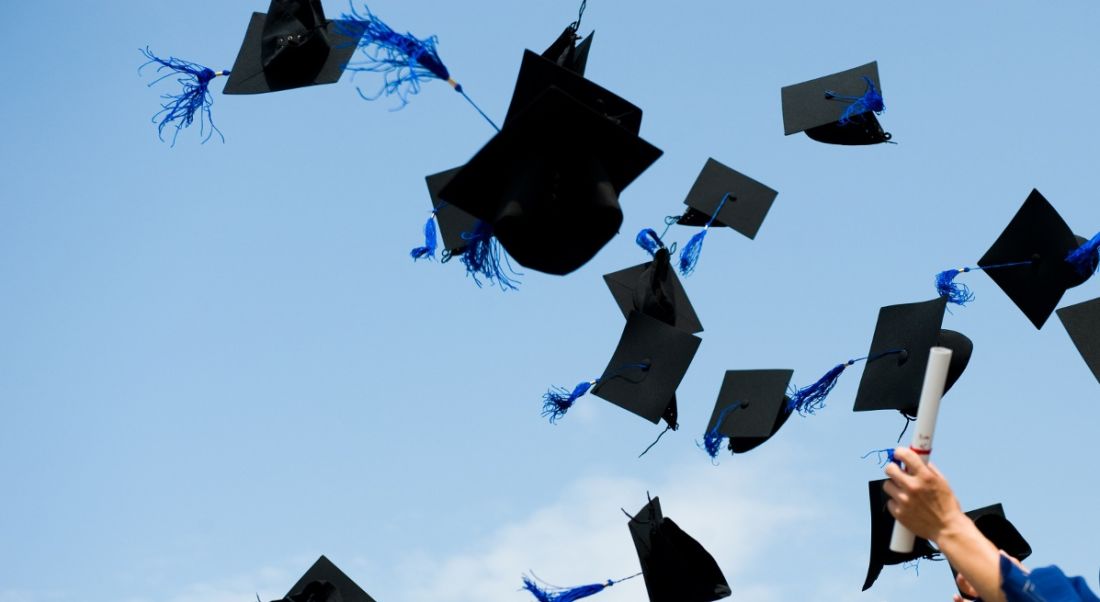 Graduates throwing their hats up in the air against a bright blue sky.