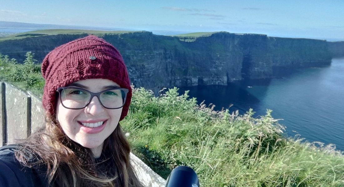 Clinical research scientist Natália Linhares is standing outside at the Cliffs of Moher and smiling into the camera.