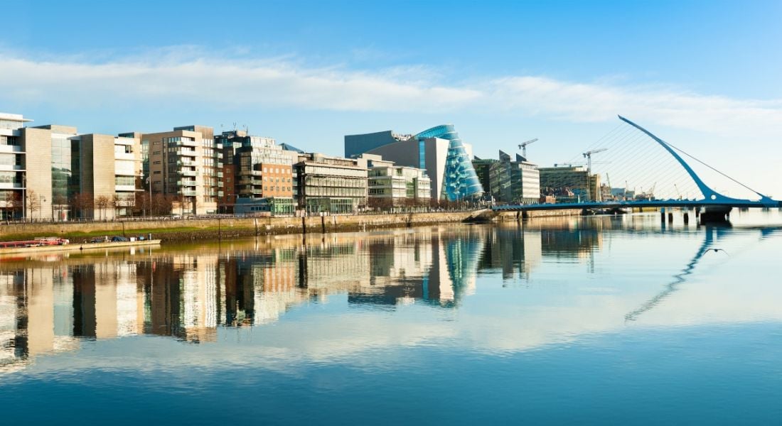 A line of office buildings along the quays in Dublin city centre with the river Liffey in the foreground and the Samuel Beckett bridge in the background.