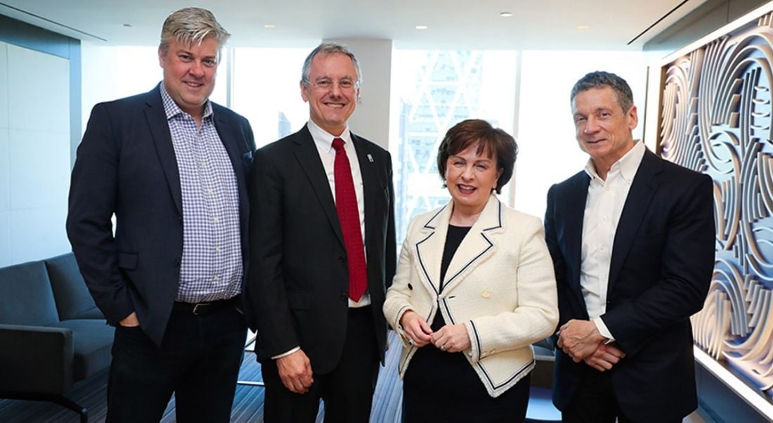 The Qarik co-founders are standing beside Kevin Holland and Diane Dodds in a brightly lit office, wearing suits and smiling into the camera.