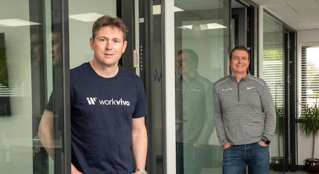 Two men in Workvivo shirts stand in a bright office space.
