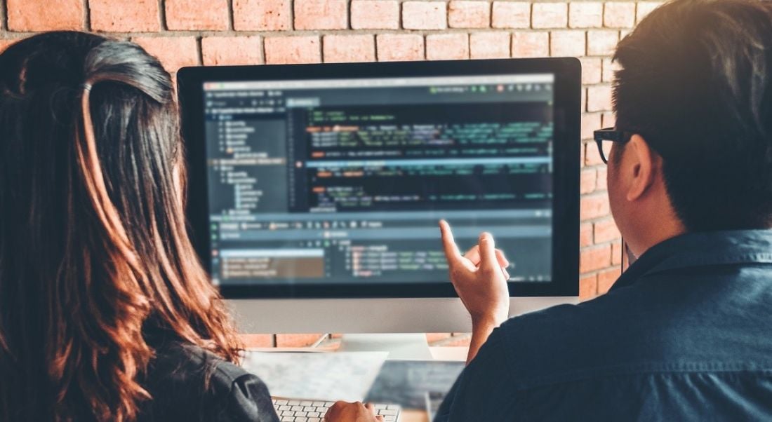 A man and a woman sit at a computer learning how to code.