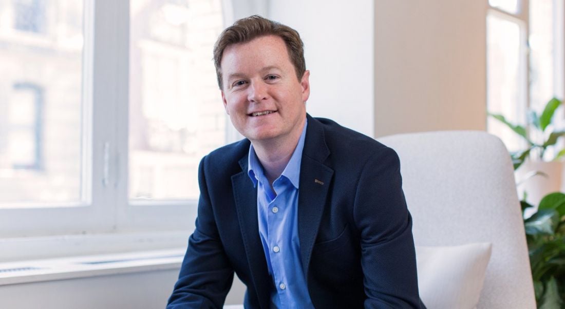 Colm O'Cuinneain, managing director of Greenhouse EMEA, is sitting in a modern, bright office, wearing a suit and smiling into the camera.