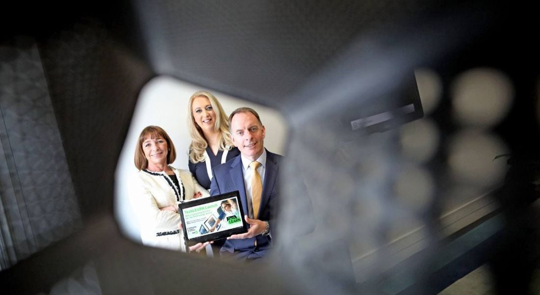 Two professional women and one man are looking into the camera down the barrel of an object. They are holding a tablet showing TechLearn, the new e-learning platform for Irish tech companies.