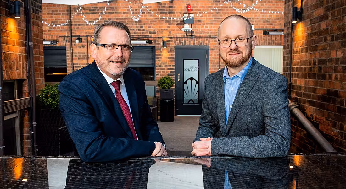 Two professional men are pictured at the Nebulon Belfast launch, standing in a modern building and looking into the camera.