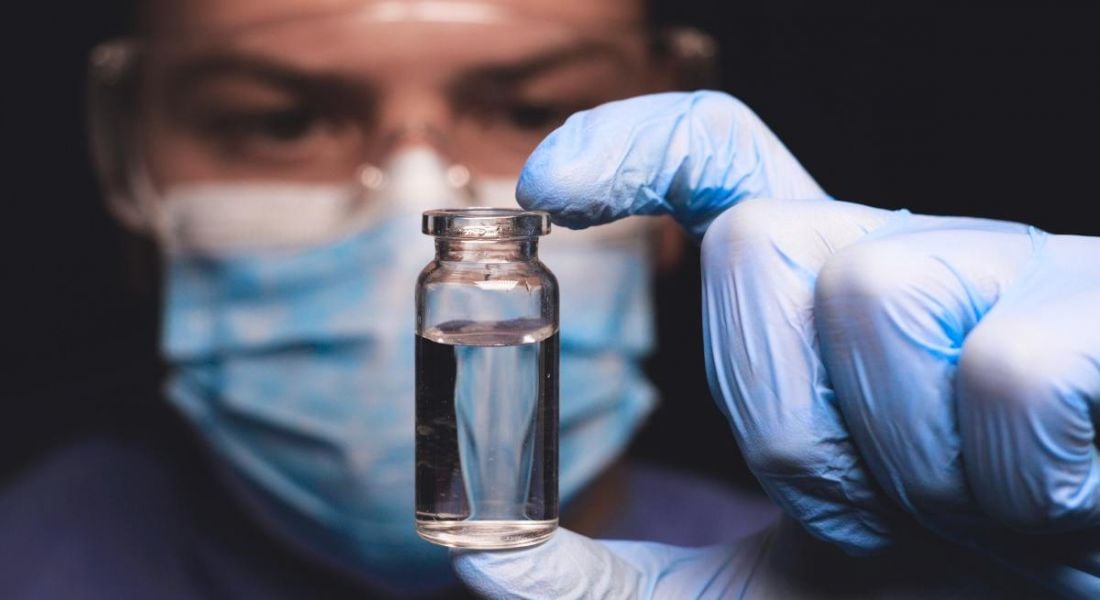 A biotech scientist is looking into a vial containing clear liquid while wearing lab gloves.