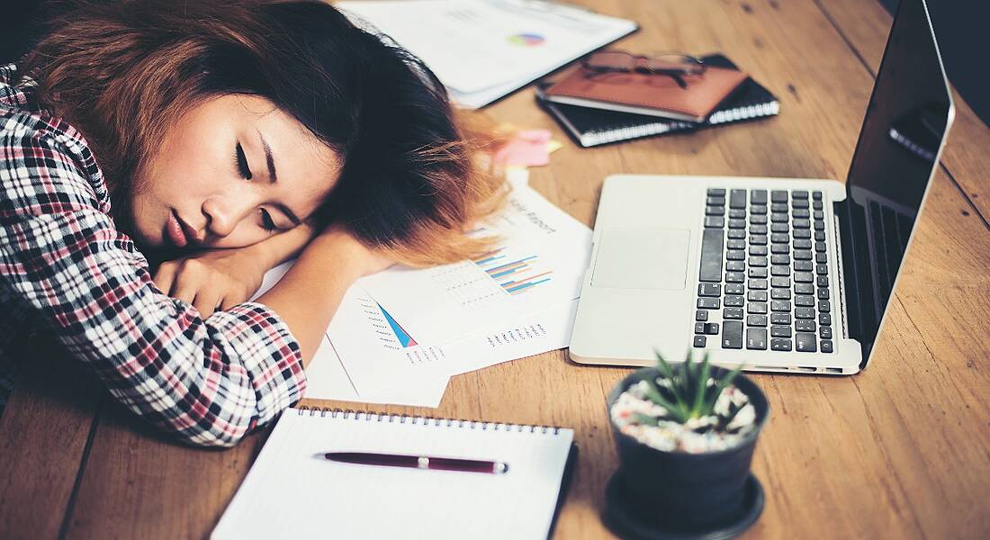 Young woman is sleeping on her desk by a laptop, showing signs of fatigue.