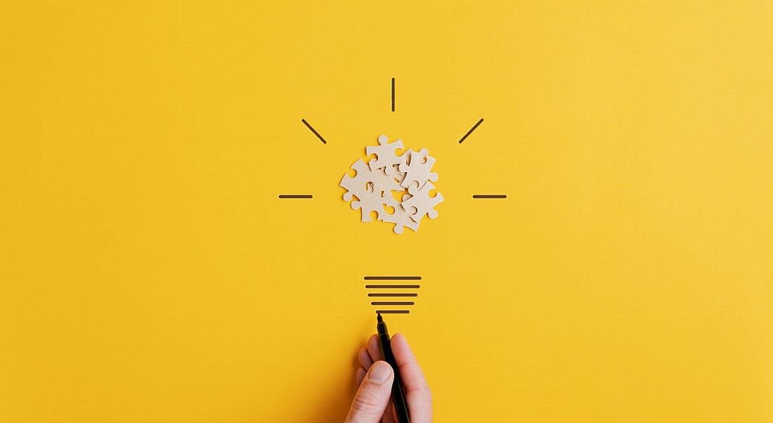 Hand drawing a light bulb of blank puzzle over yellow background.