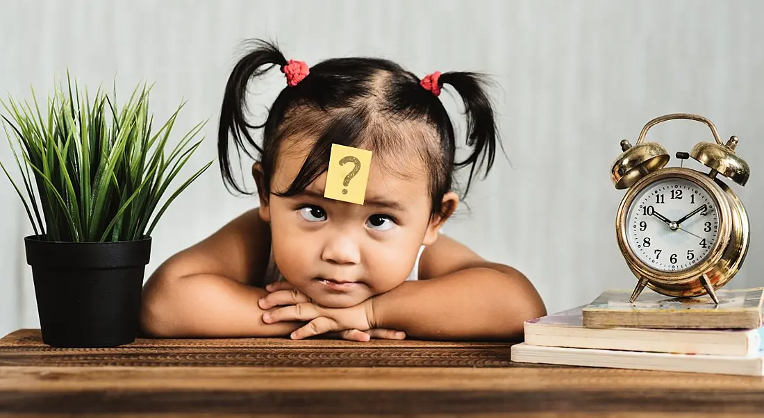 Cute and confused looking toddler with question mark on a post-it note on her forehead.