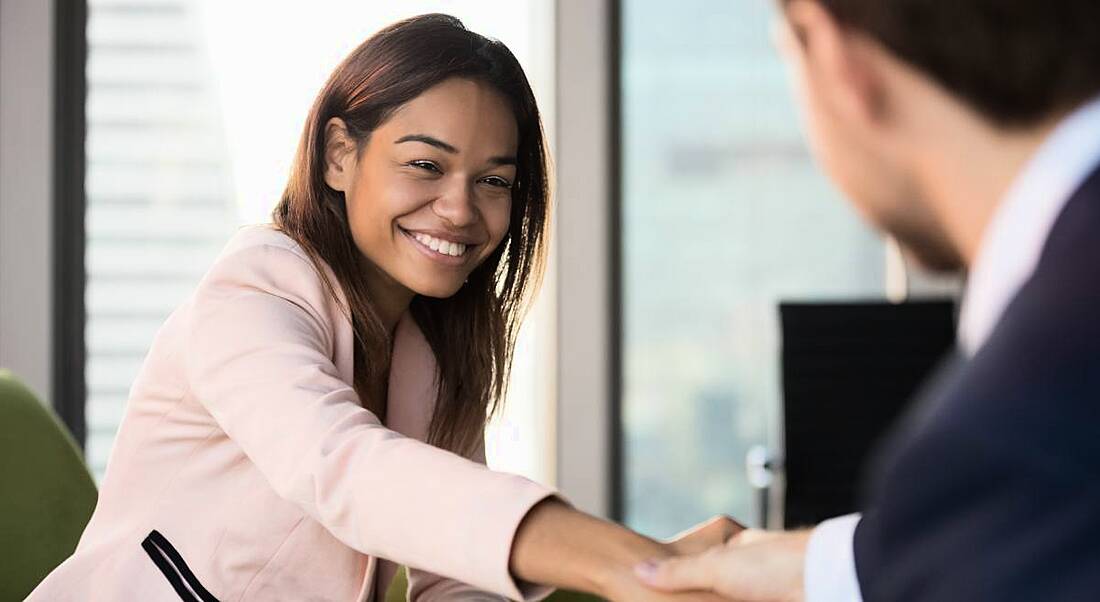 A young professional woman is shaking hands with a professional man in an interview setting.