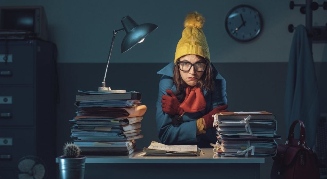 Sad woman at work, sitting at a desk in the dark wearing a coat, hat and scarf.