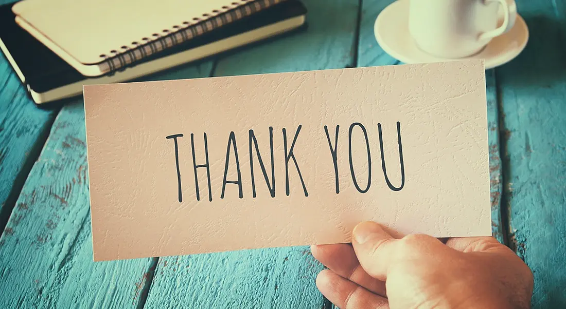 A person's hand is holding a piece of paper with thank you written on it.