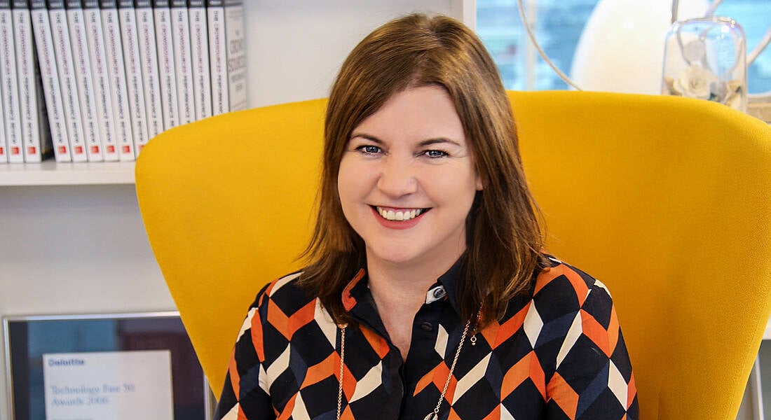 Workhuman's Michelle McDaid is sitting on a bright yellow chair and smiling into the camera at the company's Dublin office.