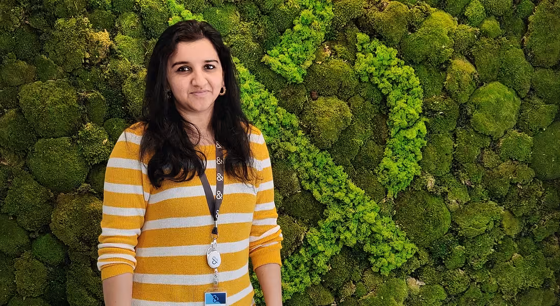 QA lead Srirekha Krishnan of Dun & Bradstreet is standing against a green wall of foliage in a bright yellow jumper and smiling into the camera.