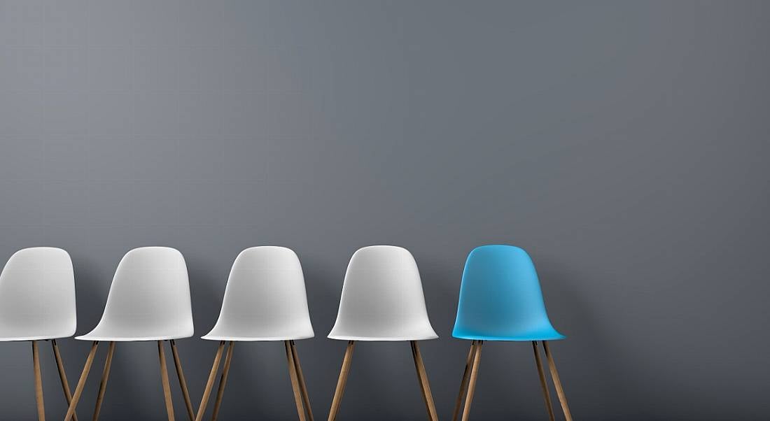 Five chairs are in a row against a grey background, with four coloured white and one coloured blue.