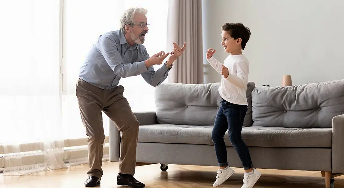 A young boy and his grandfather are dancing in a sitting room.