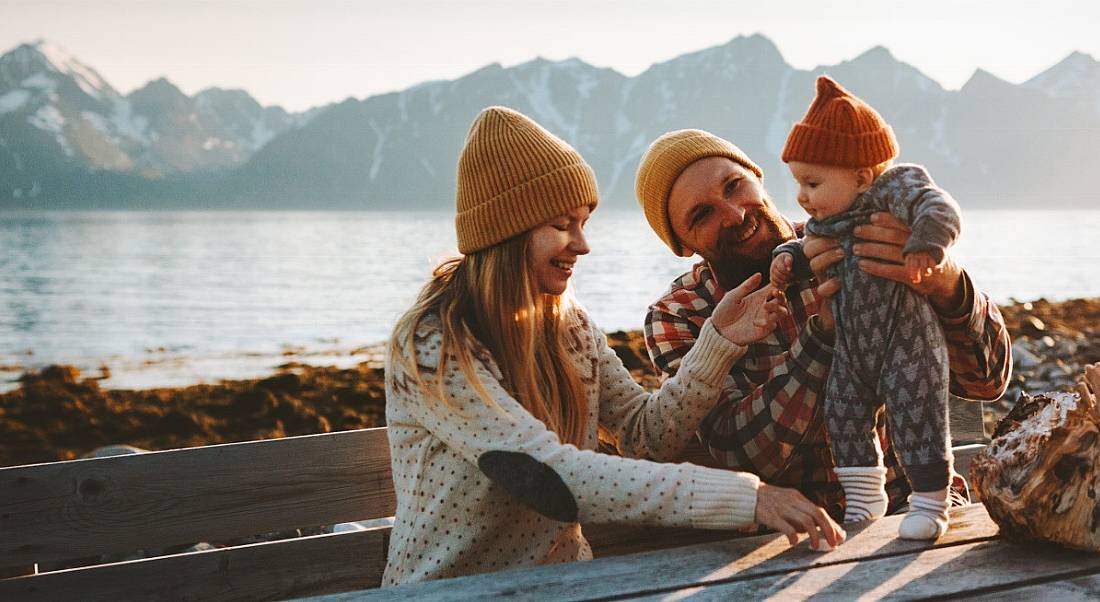 A young family of a woman and a man are interacting with their small child outside in a scenic setting.