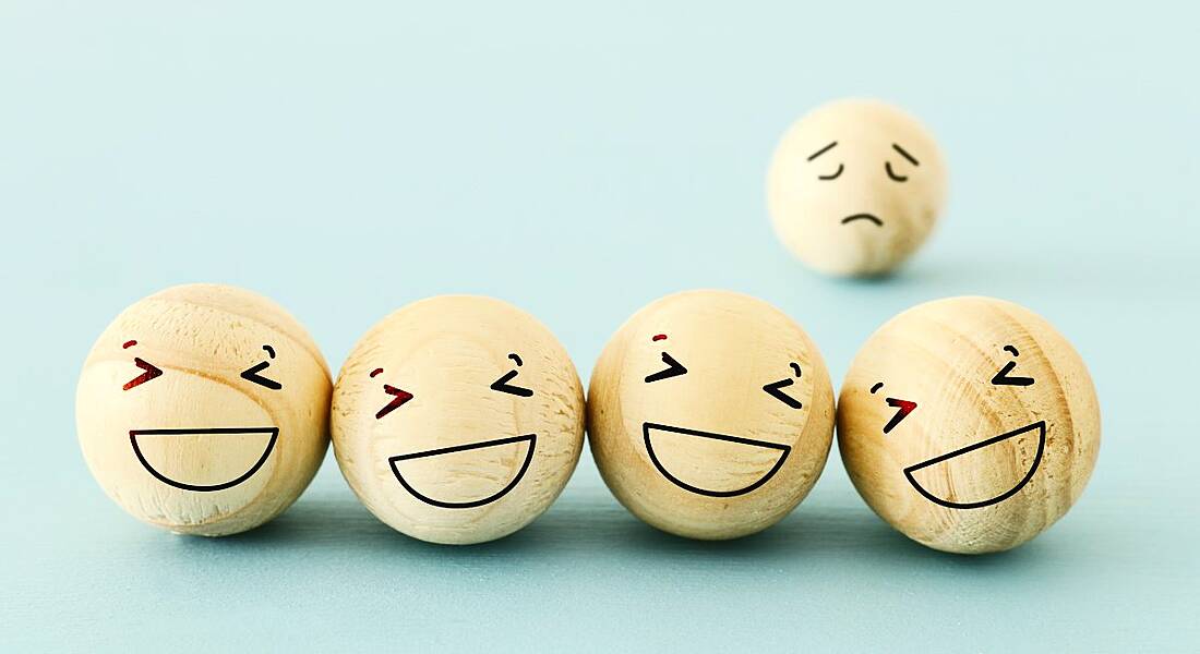 Four wooden balls with happy faces drawn on. A fifth one with a sad face is in the background, representing imposter syndrome.