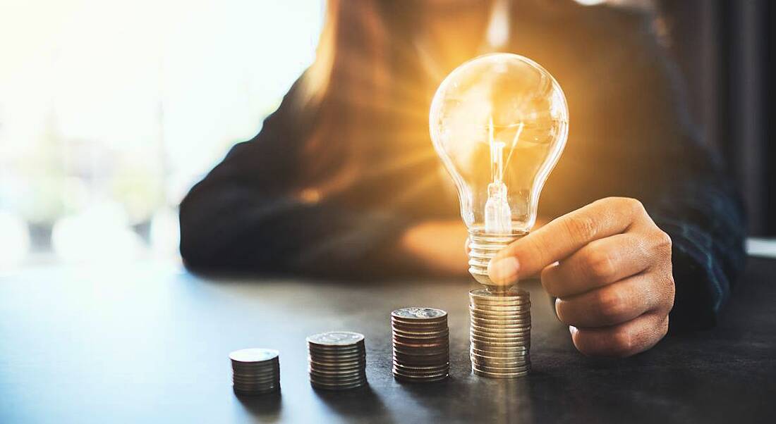 Professional woman holding and putting lightbulb on coins stack on table, representing inspiration in the financial services sector.